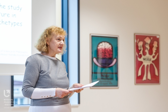 Kobieta przedstawiająca referat, wnętrze auli, barwne plakaty na ścianie